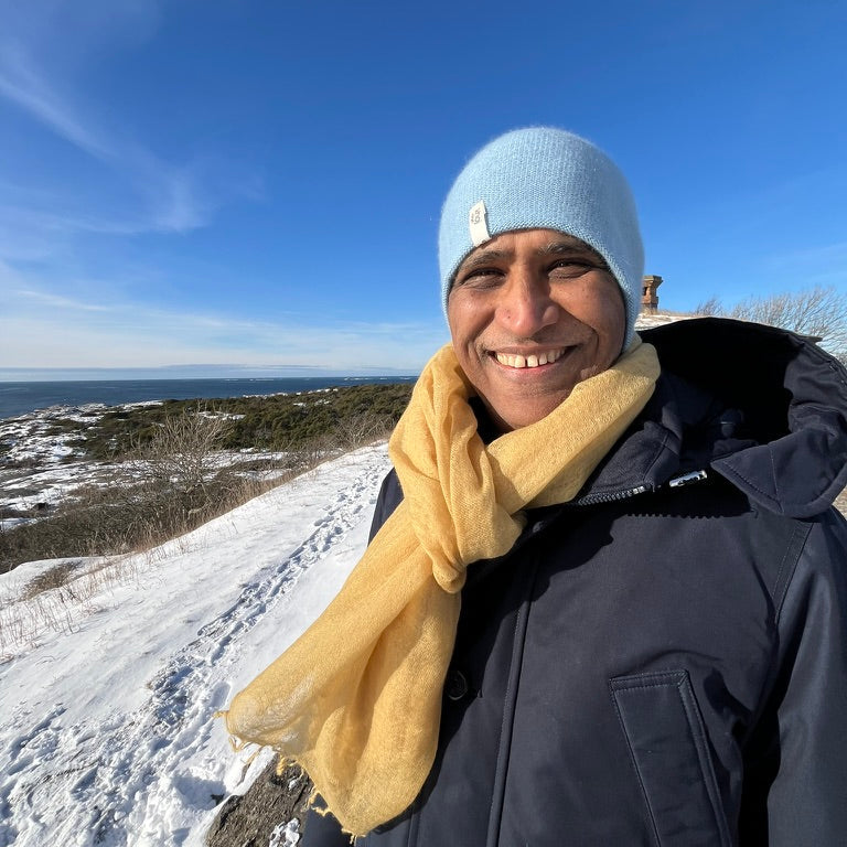 Person wearing a blue cashmere beanie and yellow cashmere scarf standing on a snowy landscape with a clear blue sky.